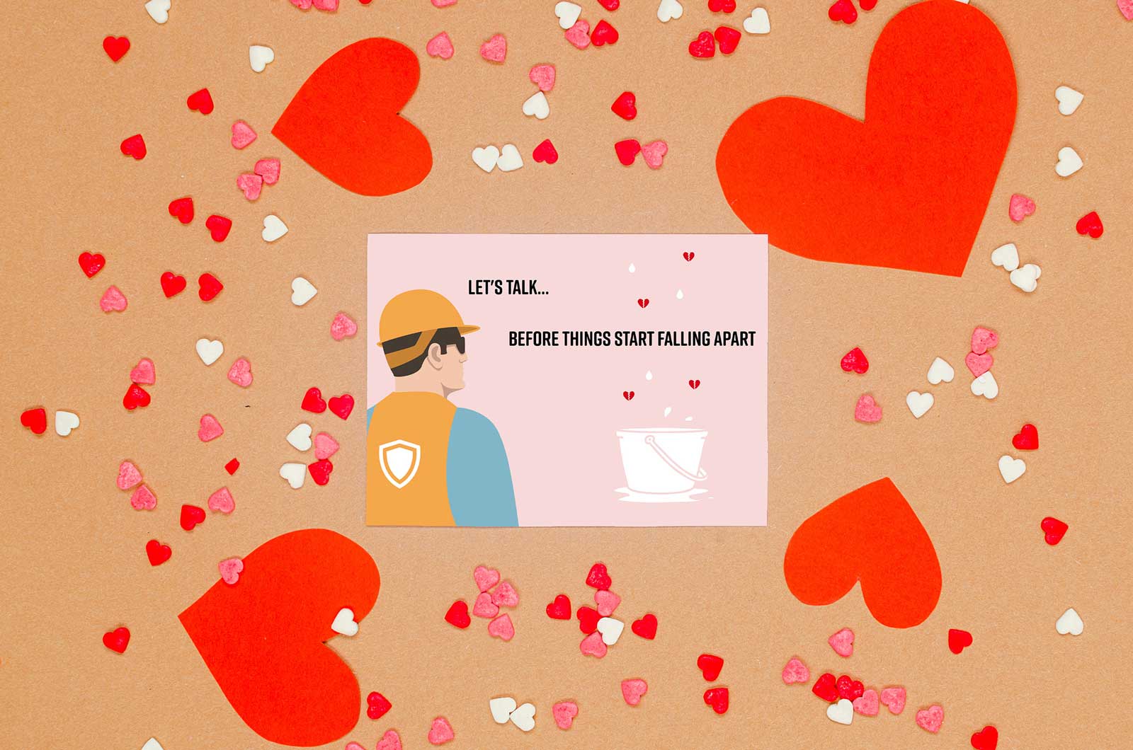 Valentine's Day card shown with heart shaped confetti. A construction worker looks at an overflowing bucket below a leak. The card reads: "Let's talk...before things start falling apart."