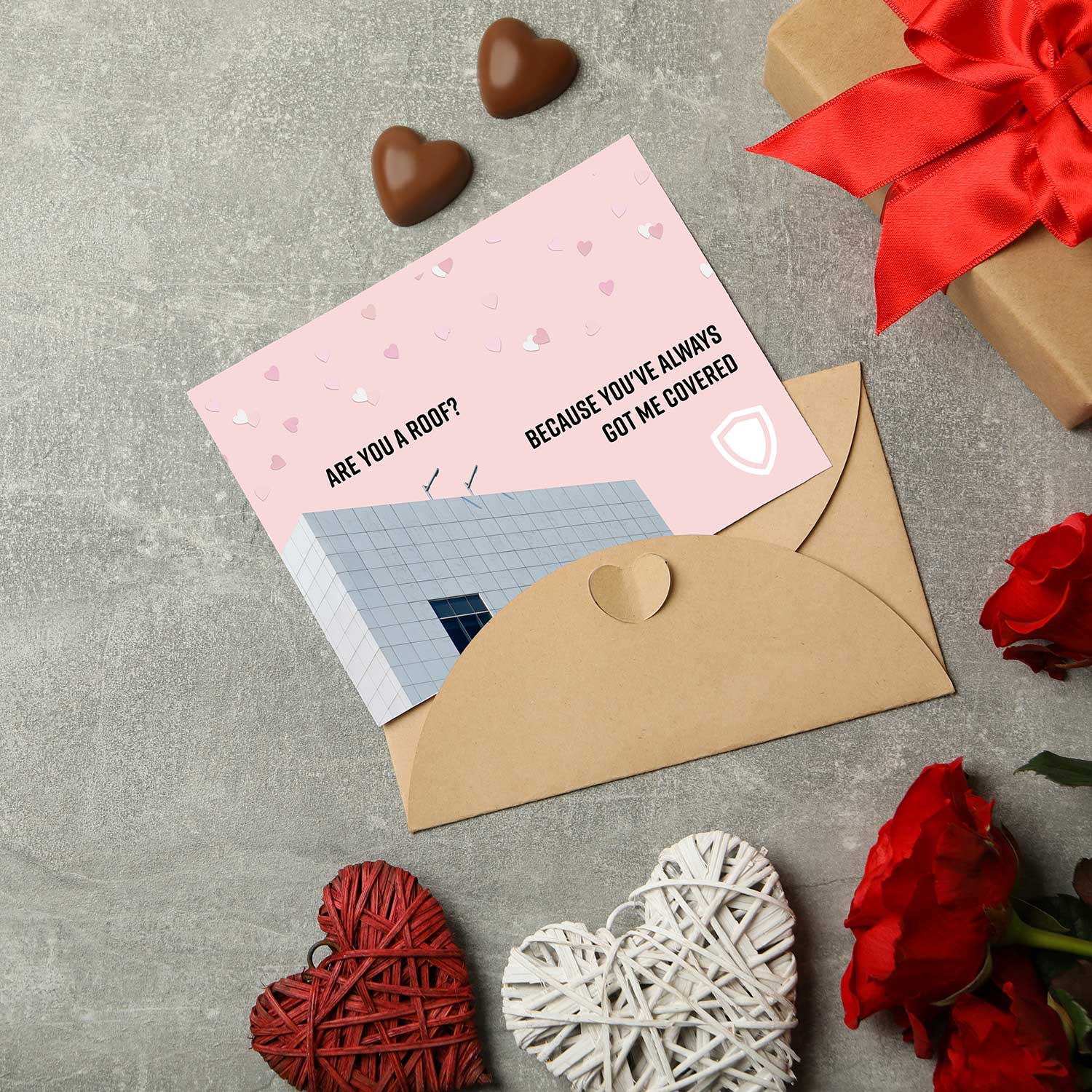 Valentine's Day card shown with chocolates and roses. The card reads: "Are you a roof? Because you've always got me covered."